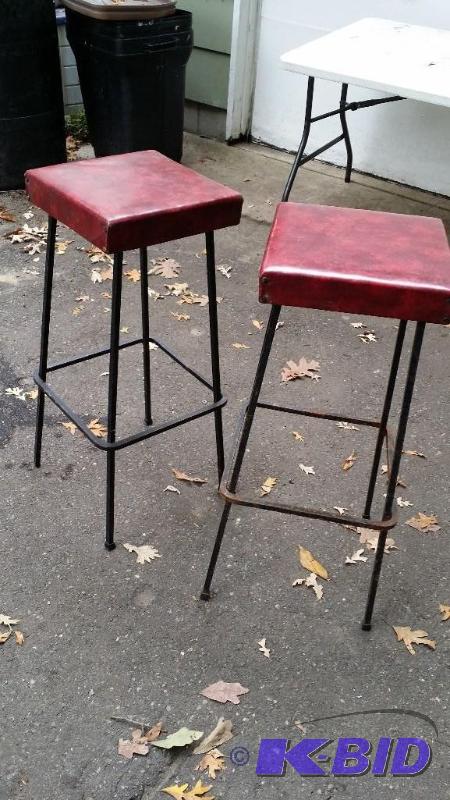 Two wrought iron stools with padded red seats...